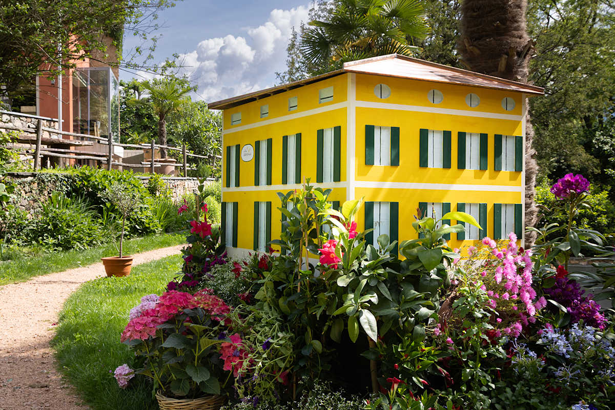 Zu sehen ist ein bunter Blumengarten in dem ein gelbes Bienenhotel steht.