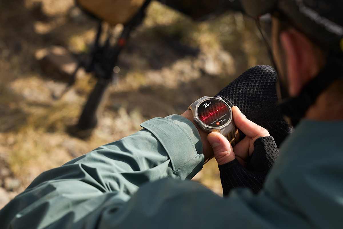 Eine Person überprüft im Freien auf ihrer HUAWEI Watch GT 6 Pro den Herzfrequenzverlauf. Die Smartwatch zeigt ein EKG-ähnliches Diagramm auf einem hellen AMOLED-Display, während im Hintergrund ein Fahrrad zu sehen ist.