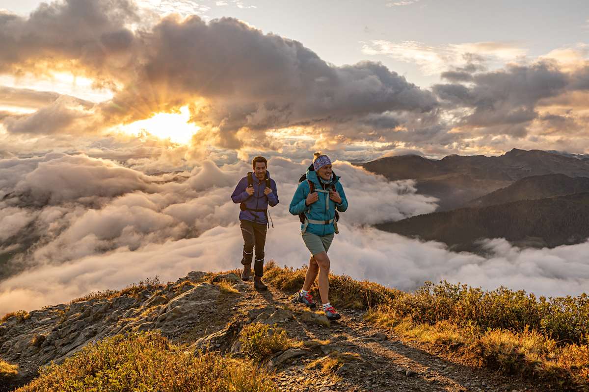 Zwei Personen mit Rucksack und Jack auf einem Bergrücken im Tiroler Alpbachtal vor spektakulärer Wolkenstimmung.