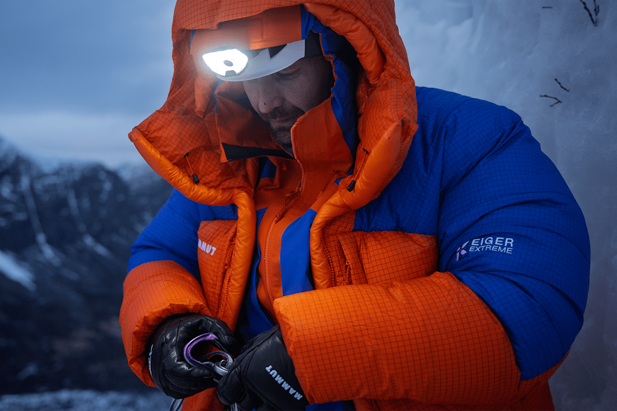 Ein Alpinist steht in den schneebedeckten Bergen und ist mit der neuen Eiger Extreme Nordwand 6.0 Kollektion von Mammut ausgestattet. Über seinem Helm trägt er eine Stirnlampe.