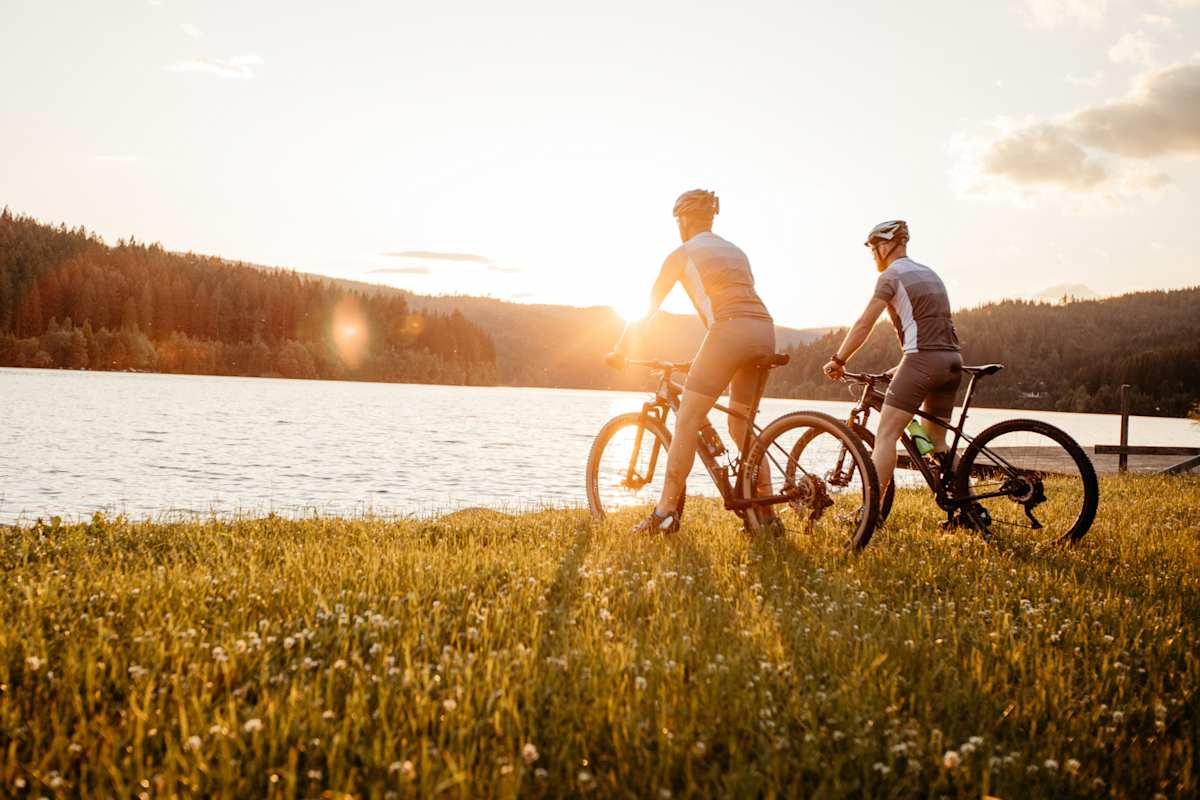 Zwei Mountainbiker genießen den Sonnenuntergang mit Blick auf einen See.