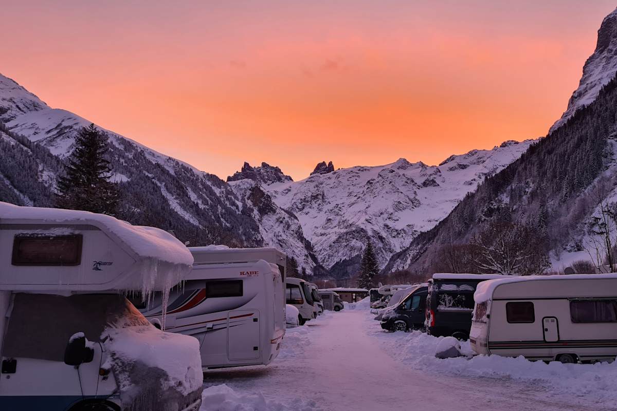 Sonnenuntergang im Alpenresort Eienwäldi Engelberg: Eingeschneite Wohnwagen und Camper stehen vor einer schneebedeckten Bergkulisse.