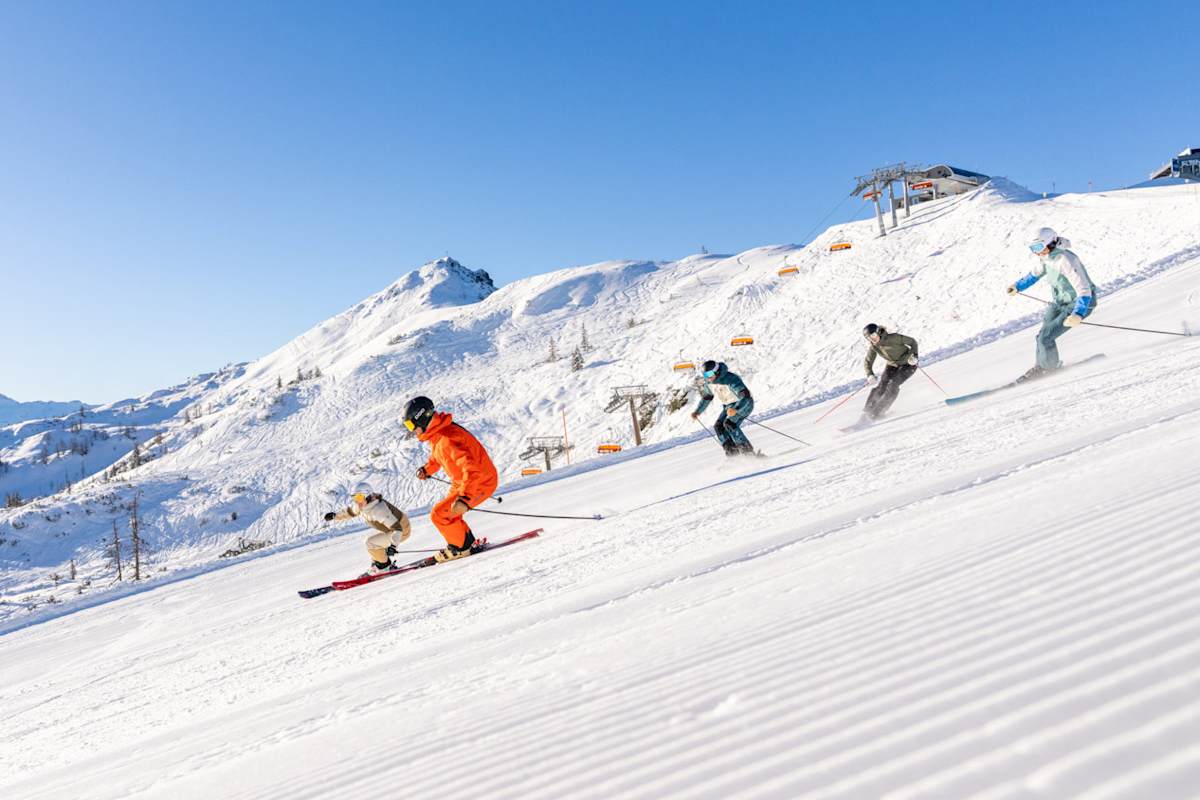Fünf Skifahrer fahren eine perfekte präparierte Piste in Flachau hinunter.