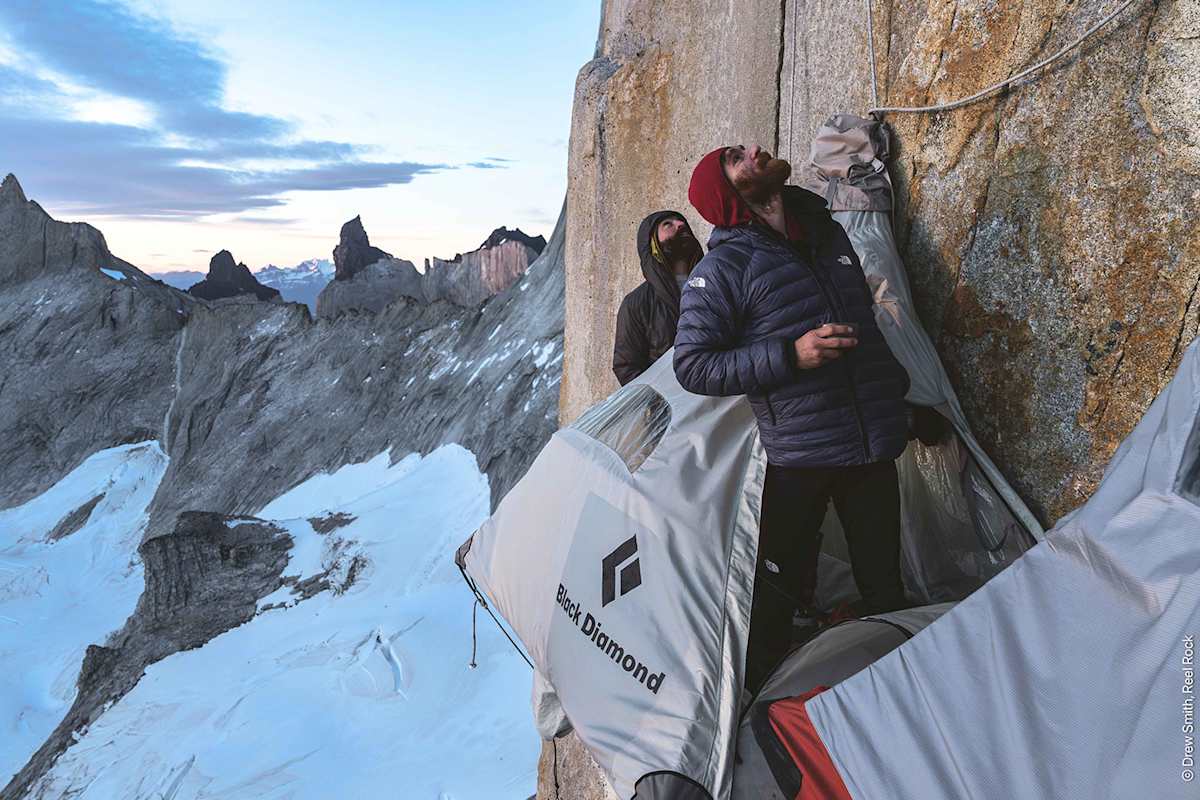 Zwei Männer hängen an einer Felswand und blicken in den Himmel.