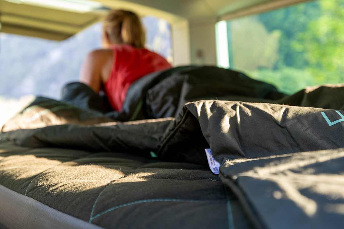 Eine Frau liegt in ihrem Van auf einer Matratze.