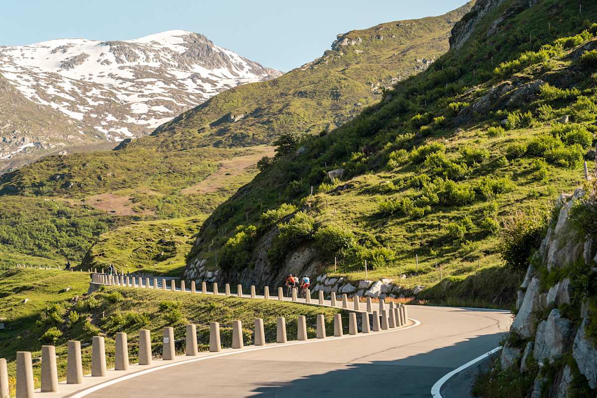Schneeberge, grüne Hügel und Radfahrer auf dem Asphalt im Sommer.