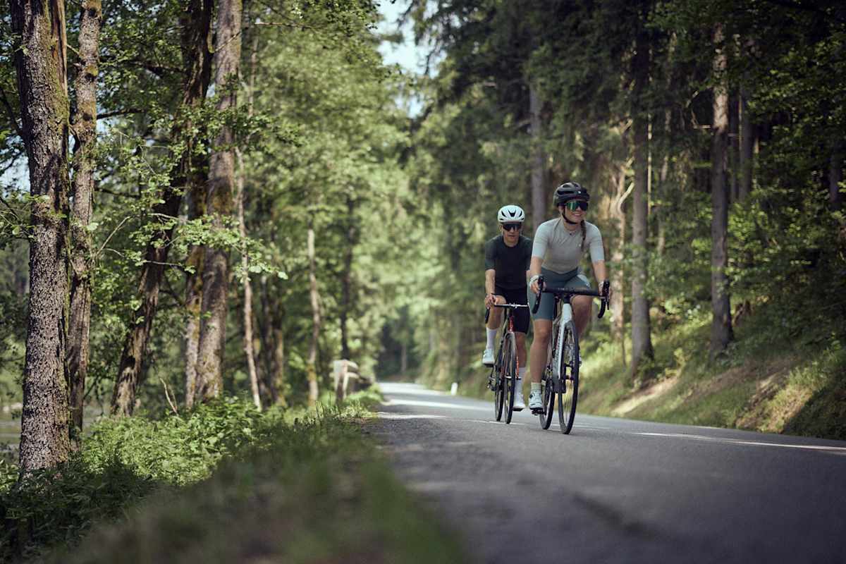 Eine Frau und ein Mann fahren im Wald neben einem Fluss Fahrrad