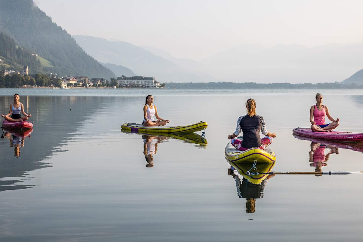 Vier Frauen sitzen mit verschränkten Beinen auf ihren SUPs und meditieren auf dem See.