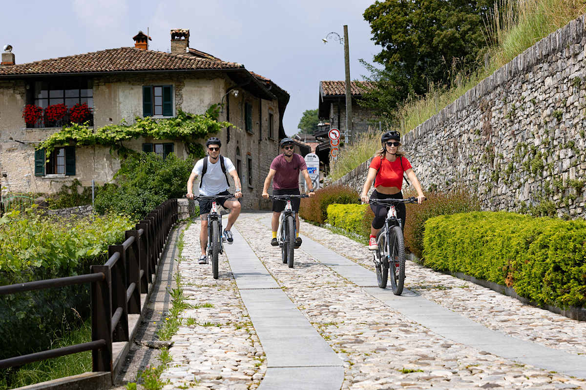 Drei Personen fahren auf einem Fahrrad durch ein kleines Städtchen.
