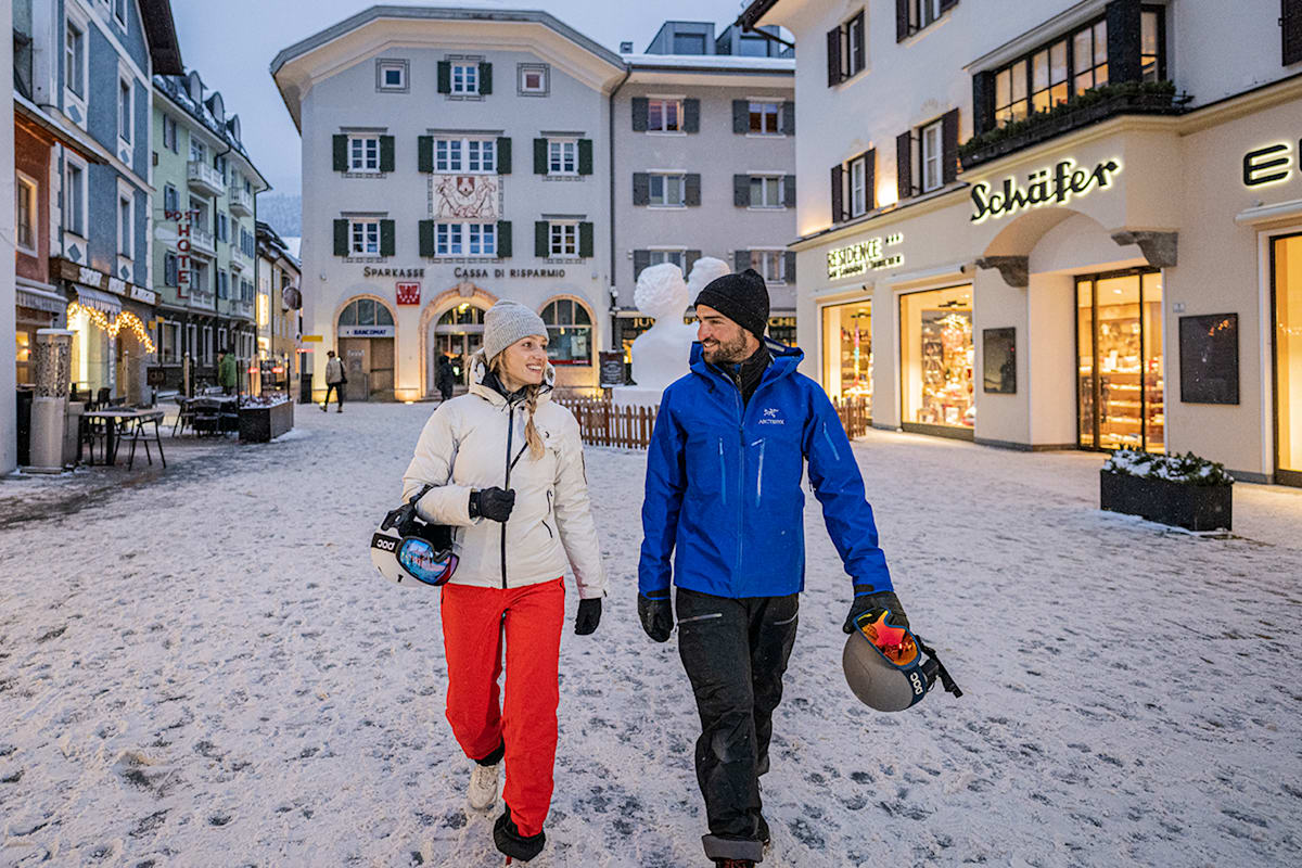 2 Personen in der Stadt Innichen im Winter mit Skiausrüstung.