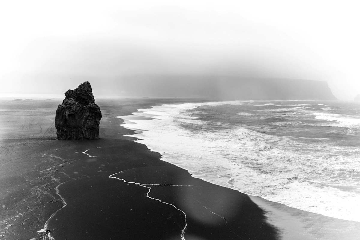 Einsamer Felsturm am Reynisfjara, dem Schwarzen Strand an der Südküste mit aufgewühltem Meer und nebligem Himmel