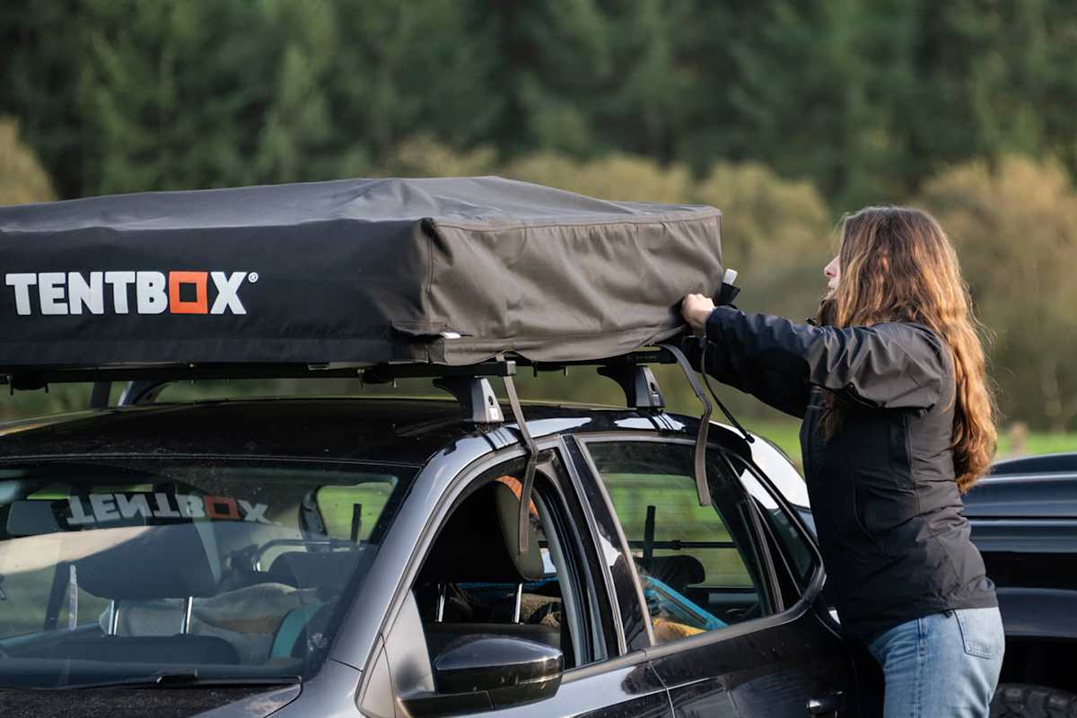 Eine Frau verstaut ein Dachzelt in seiner Aufbewahrung auf dem Dach des Autos.