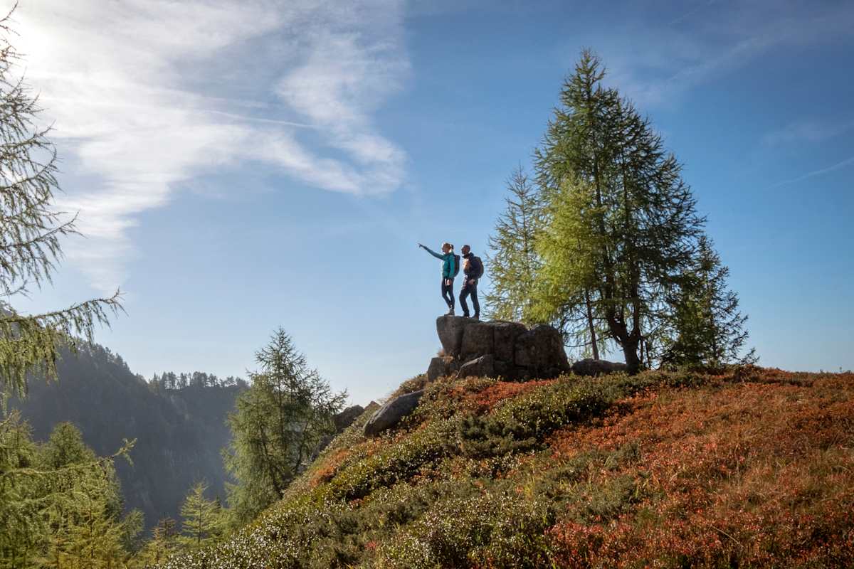 Zwei Wanderer stehen auf einem Felsen und deuten in die Ferne.