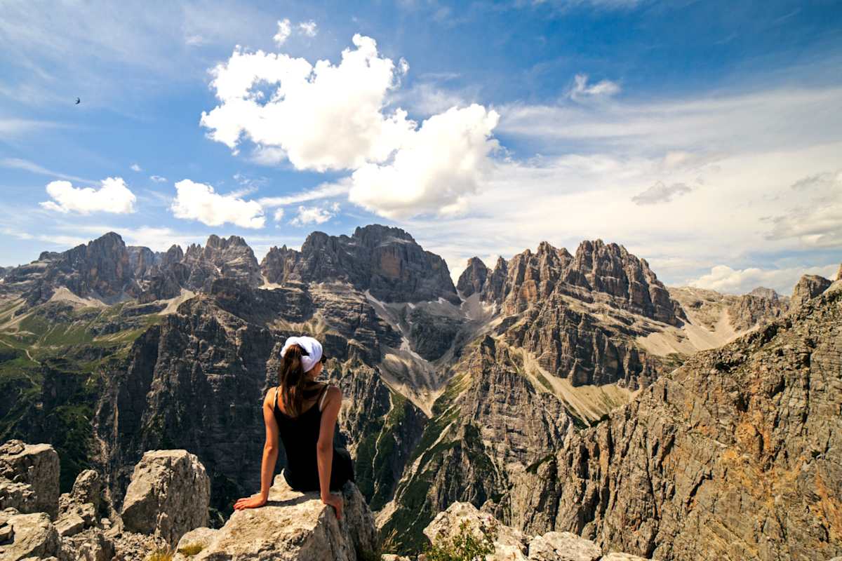 Eine Frau sitzt auf einem Felsen und genießt das gewaltige Panorama über die Brenta-Dolomiten.
