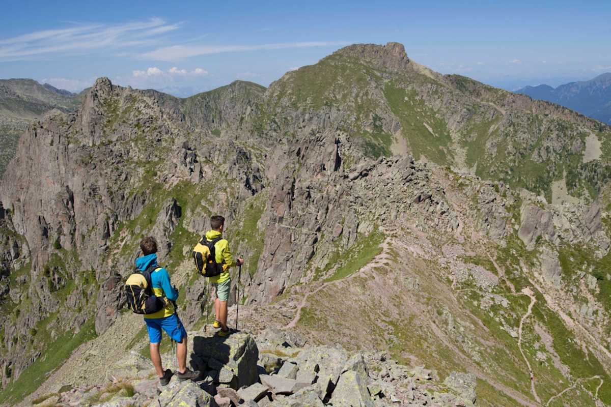 Zwei Wanderer mit Stöcken schreiten über das rote Porphyrgestein des Monte Cauriol.