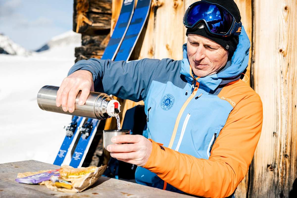 Mann trinkt Tee vor Hütte im Winter