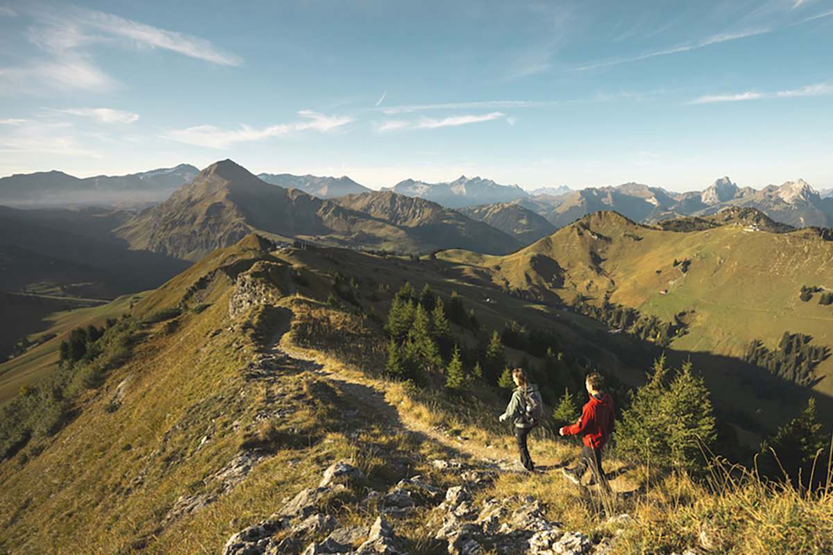 Wanderer auf einem Berggrat in der herbstlichen Alpenlandschaft von Gstaad mit Blick auf die umliegenden Gipfel.