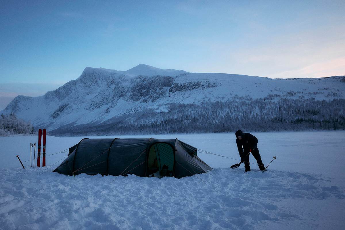Wintercamping in verschneiter Berglandschaft, perfekt ausgerüstet mit Haglöfs Outdoor-Bekleidung und -Ausrüstung.