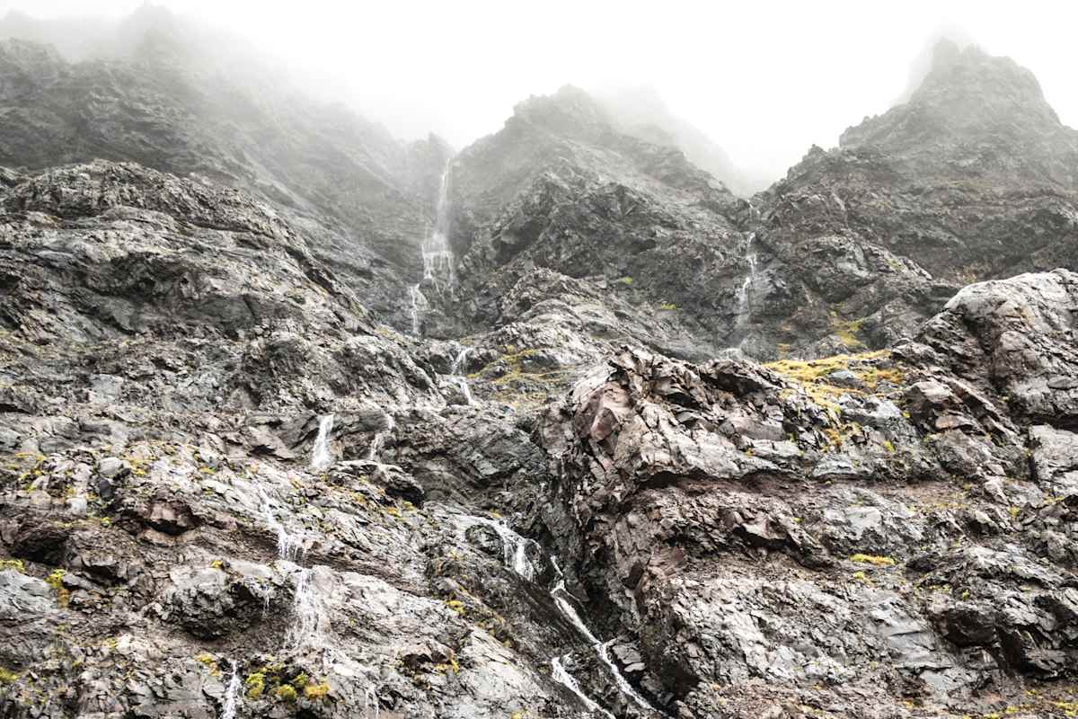 Karges Gestein und kleine Wasserfälle vor nebligem Himmel