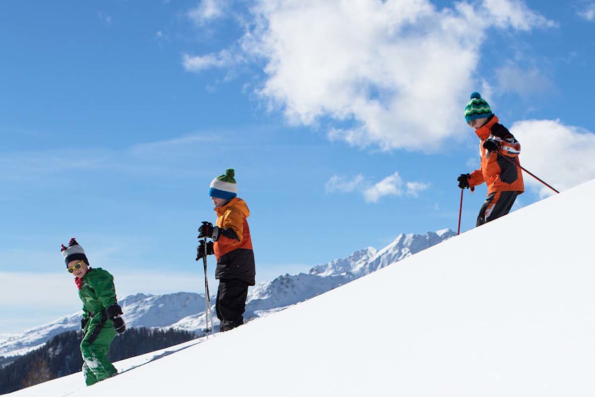 Kinder fahren mit den Skiern den Hang hinunter.