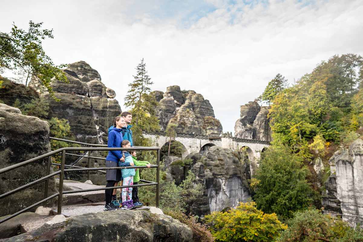 Eine Familie wandert auf dem Malerweg zwischen Sandsteintürmen und schaut in die Ferne.