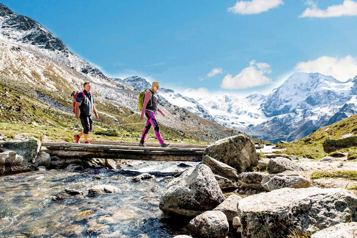 Wanderer überqueren einen Gebirgsbach, schneebedeckte Berge im Hintergrund