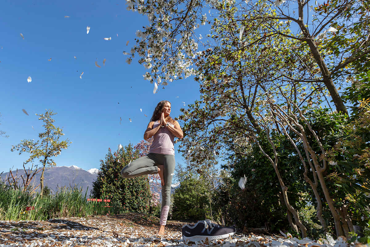 Zu sehen ist eine Frau in Sportkleidung die inmitten von Bäumen eine Yogaposition einnimmt.