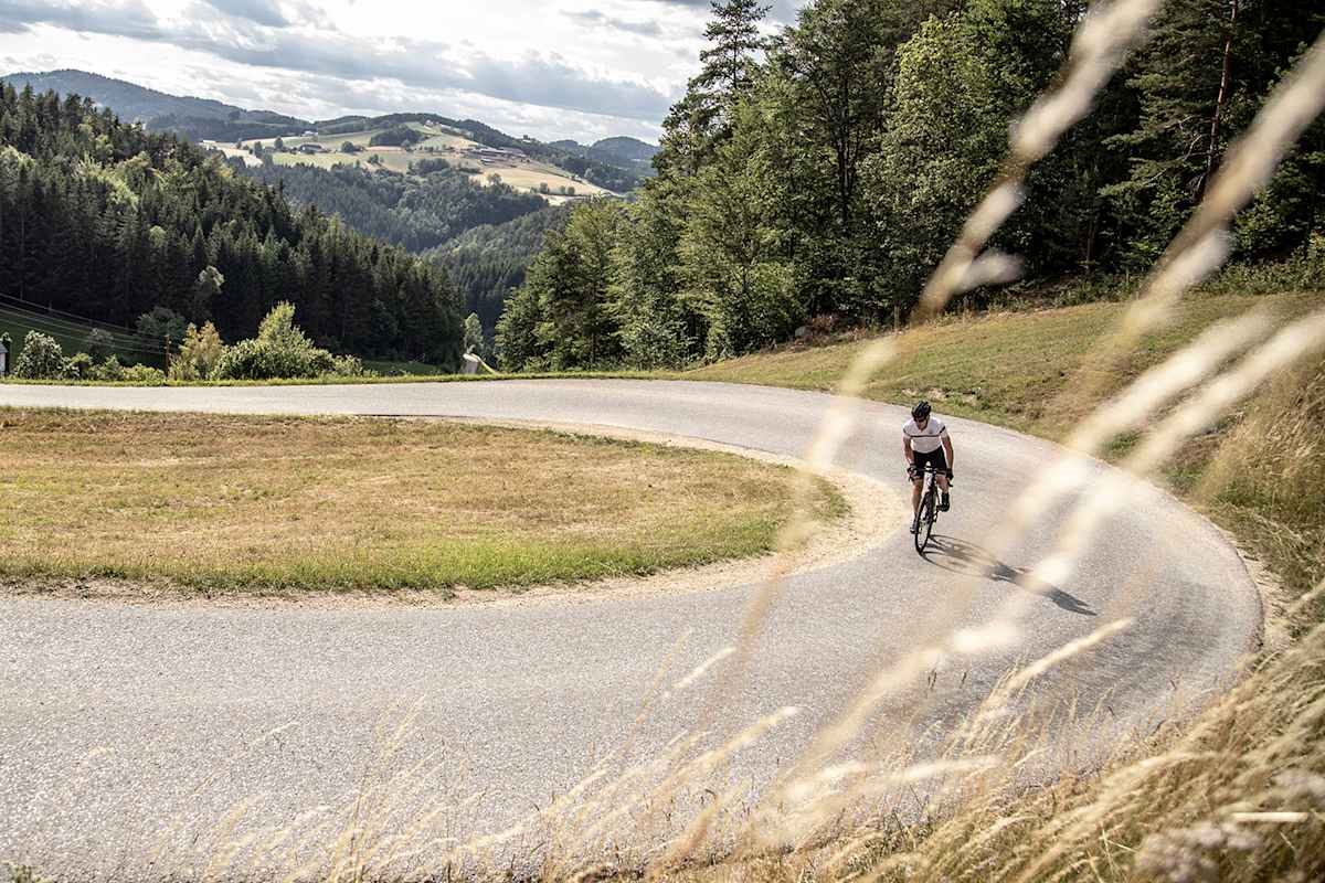 Radfahrer in weiter Kehre im Mühlviertel, umgeben von Hügeln und Waldlandschaft.