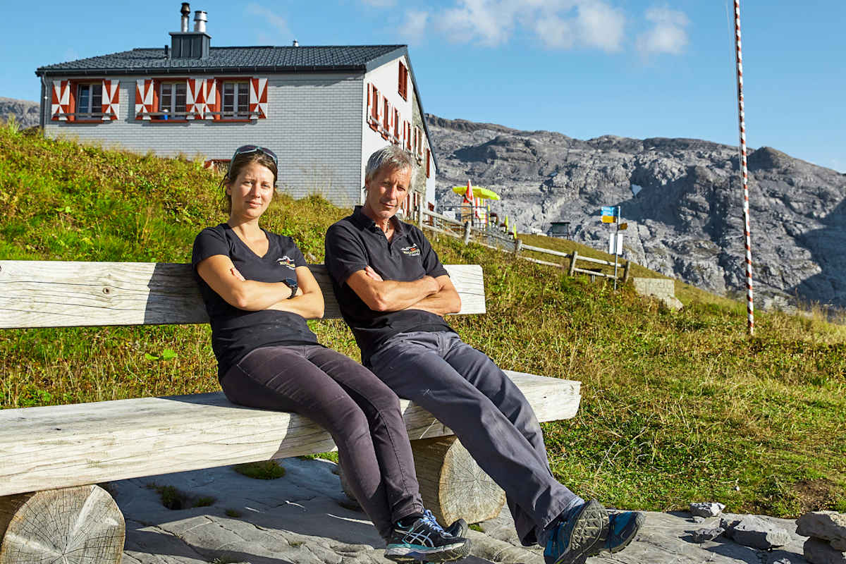 Die Hüttenbetreiber sitzen auf einer Bank vor der Hütte.