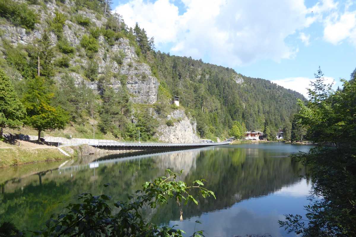 Ein grüner See, der rechts von Bäumen und links von einer Felswand eingerahmt ist.