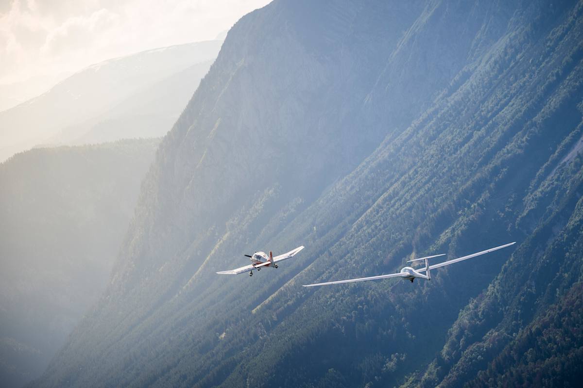 Zwei Flugzeuge vor nebelverschleierten Bergen.