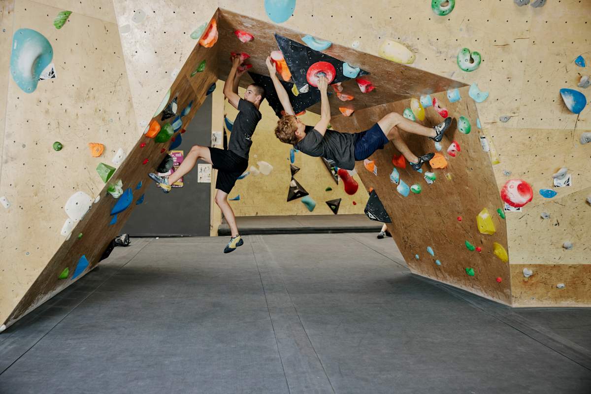 Zwei Boulderer hängen in der Halle an bunten Griffen