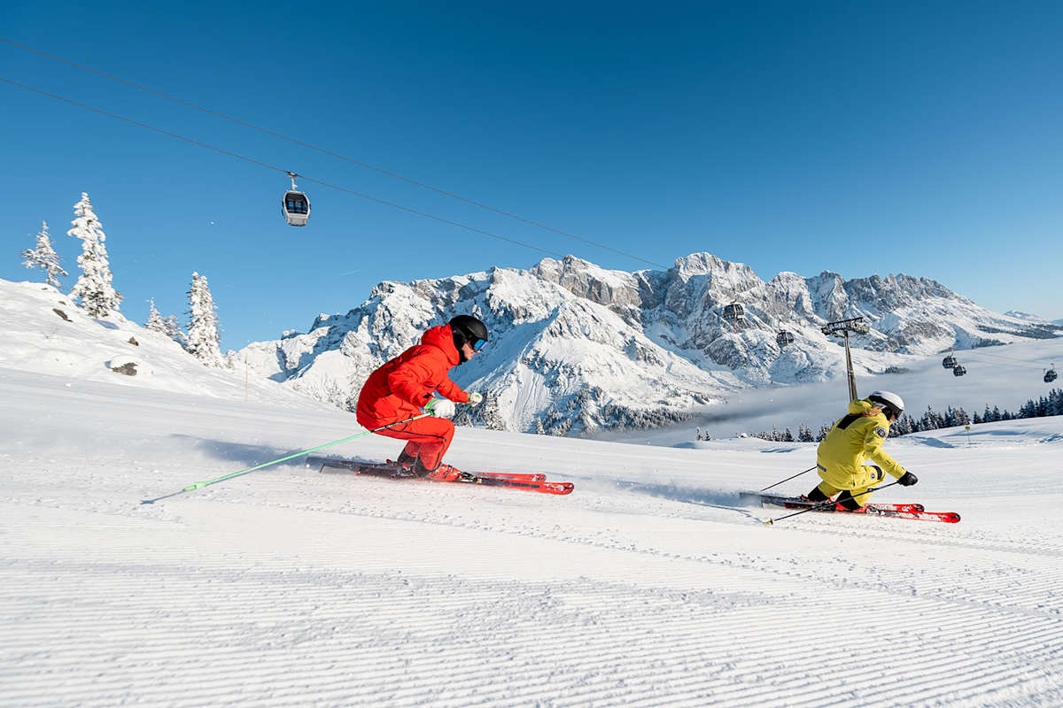2 Skifahrer auf der Piste fahren den Hang herunter.