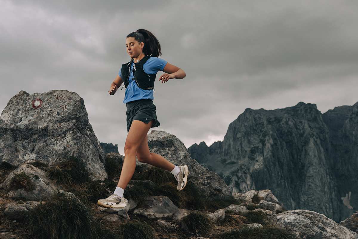 Eine Frau befindet sich auf einem Trailrun in einer grauen, alpin-felsigen Landschaft und trägt eine Trailweste von Rab.