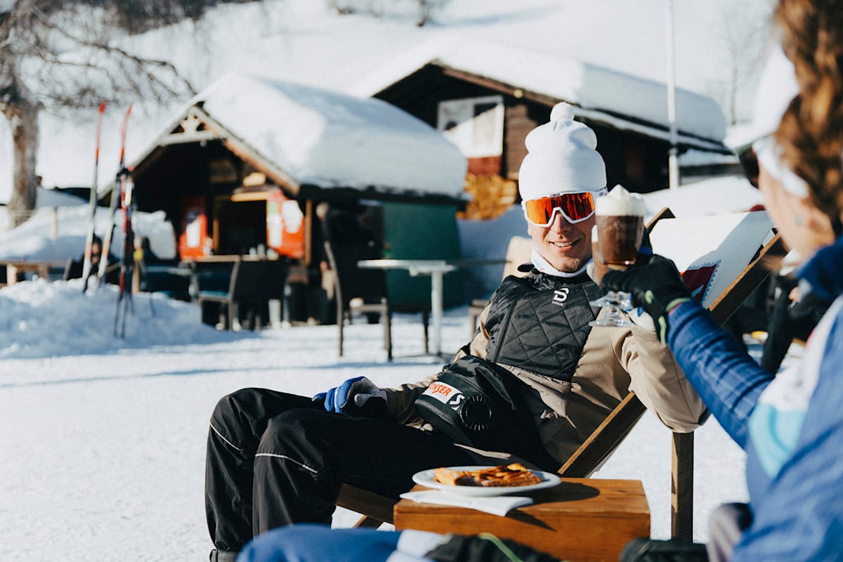 Ein Paar sitzt im Schnee und trinkt heiße Schokolade.