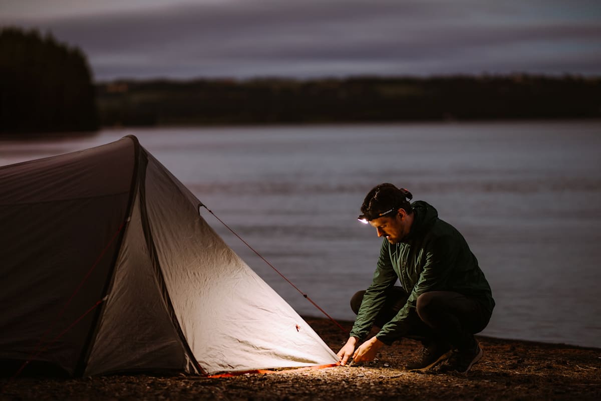 Manns schlägt in der Dämmerung ein Zelt auf und beleuchtet die Situation mit der Supreabeam V7.