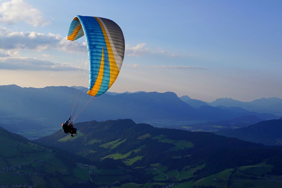 Ein Tandemflug von zwei Personen mit einem Paragleitschirm vor alpiner Kulisse.