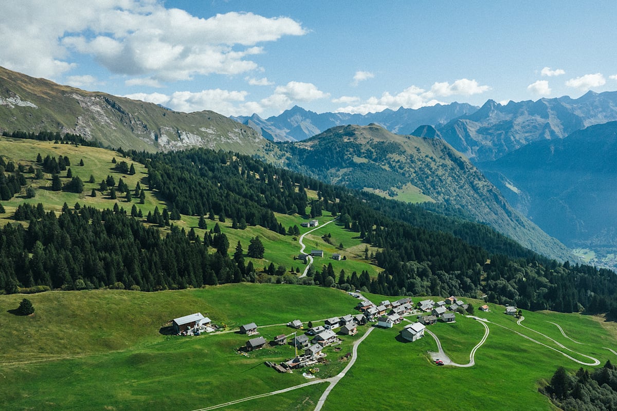 Ein Bild von einer Ortschaft in den Schweizer Alpen und rundherum viele Wälder, Wiesen und Berge.