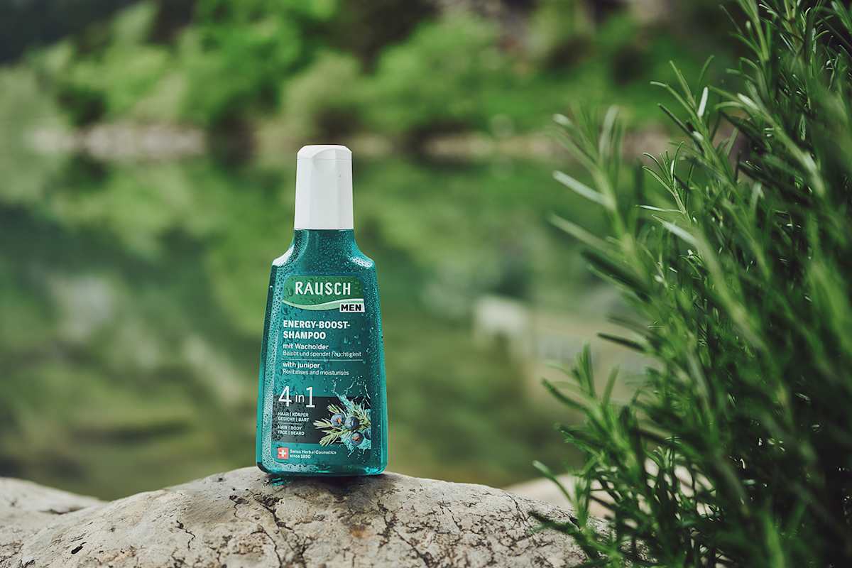 Zu sehen ist eine türkise Flasche RAUSCH Energy-Boost-Shampoo vor einem grünen Hintergrund.