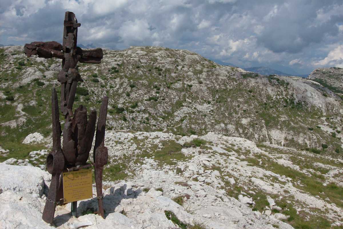 Ein Gipfelkreuz aus verrosteten Metallresten vor einem kargen, steinigen Bergplateau.