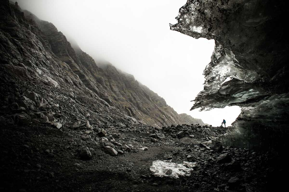 Mensch steht in Trogtal aus dunklem Gestein vor weißem Himmel
