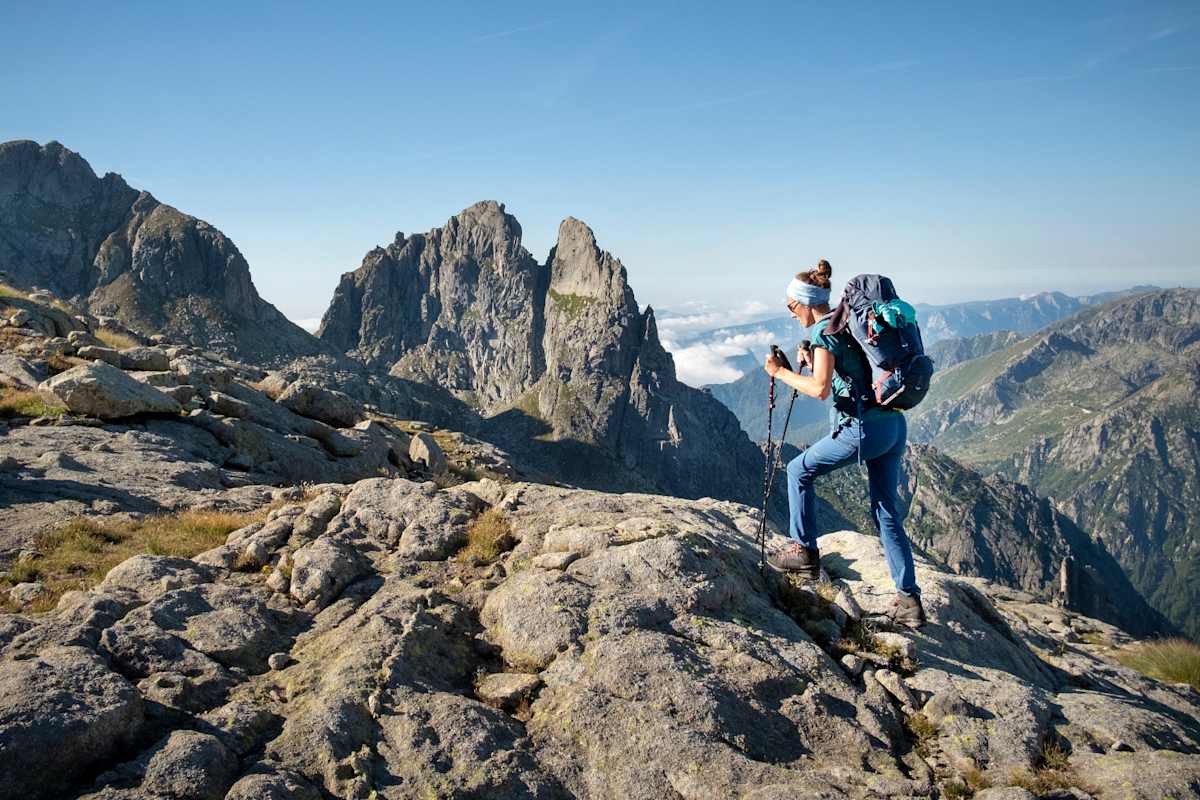 Eine Wanderin geht mit Stöcken in den Händen über ein steiniges Gipfelplateau im Trentino.