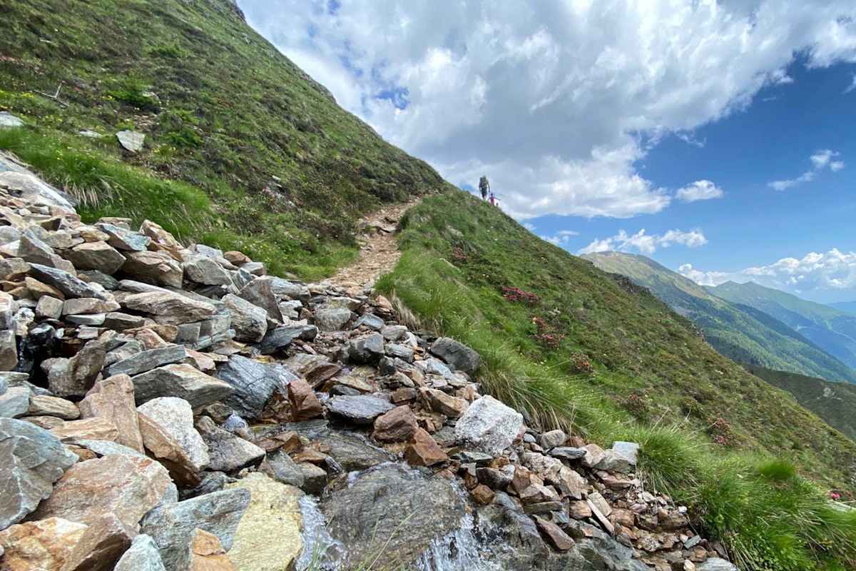 Im Vordergrund ein Steinhaufen, im Hintergrund zwei Wanderer am Horizont