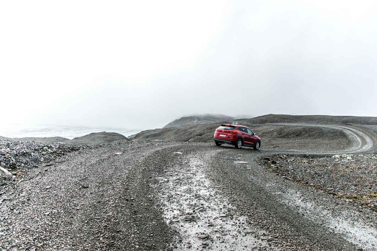 Rotes Auto auf isländischer Bergstraße bei nebligem Wetter