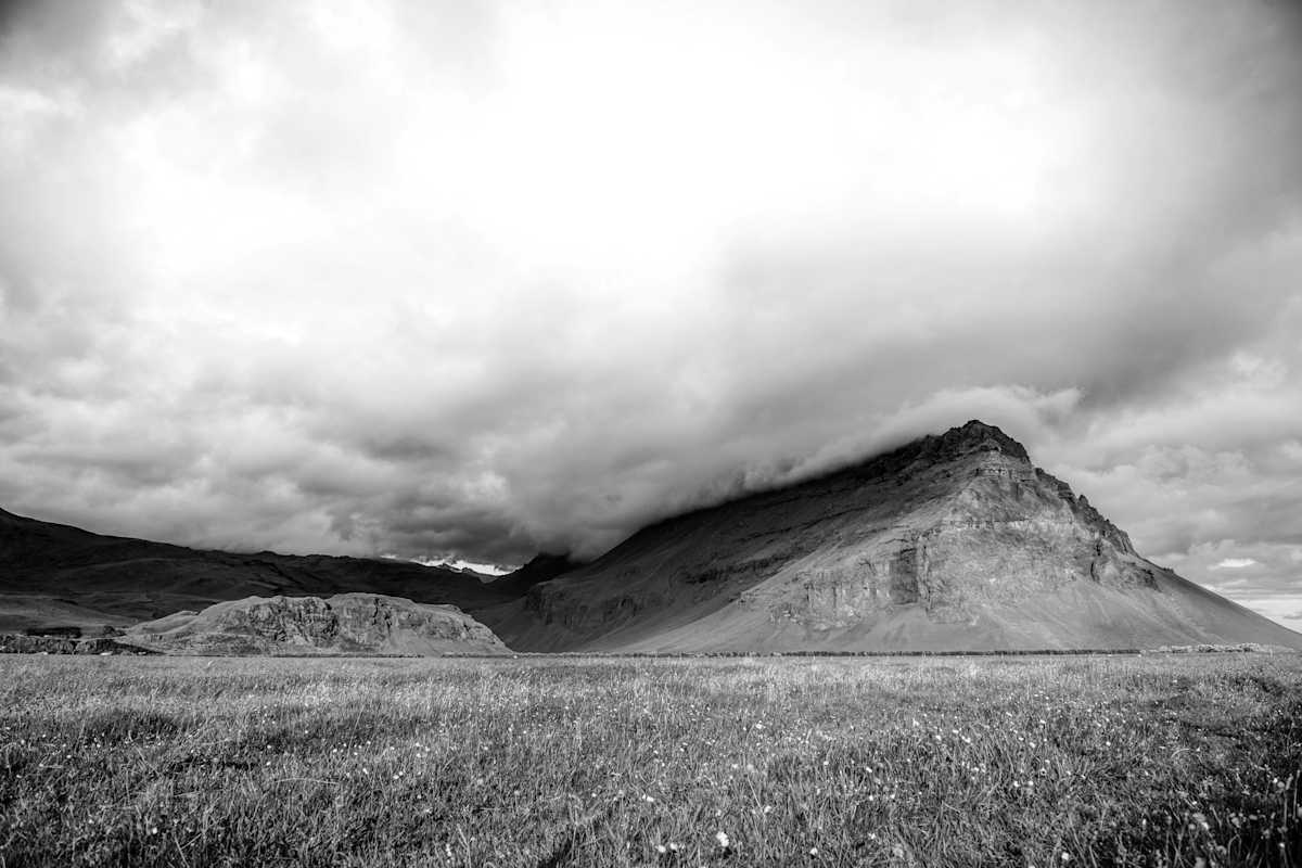 Eine Wiese vor karger Berglandschhaft mit dunklen Wolken, welche sich über den Bergen türmen.