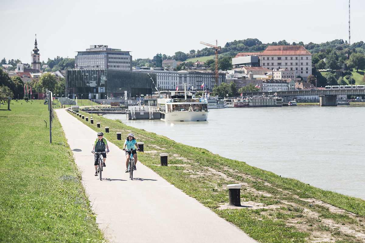 Der Donauradweg bei Linz lädt zum Radeln am Wasser mit Stadtpanorama ein.