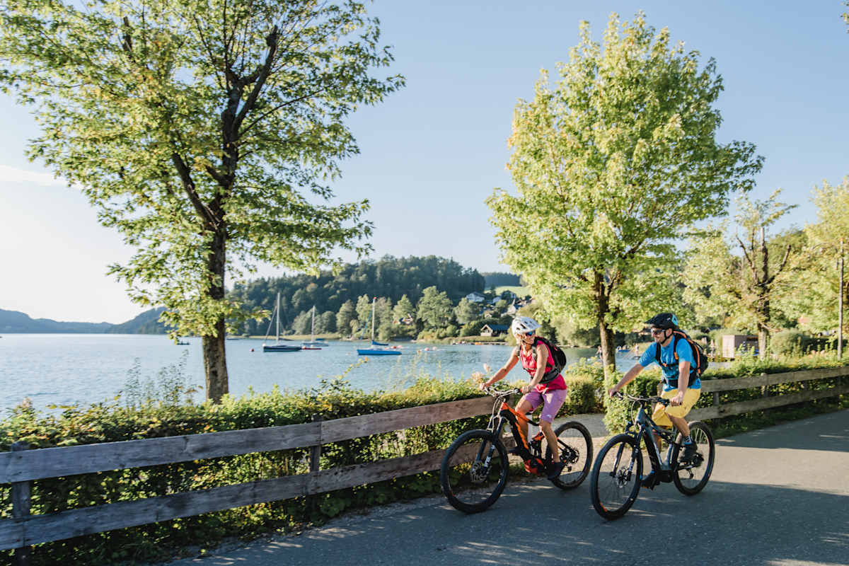 Zwei E-Biker fahren an einem See entlang.