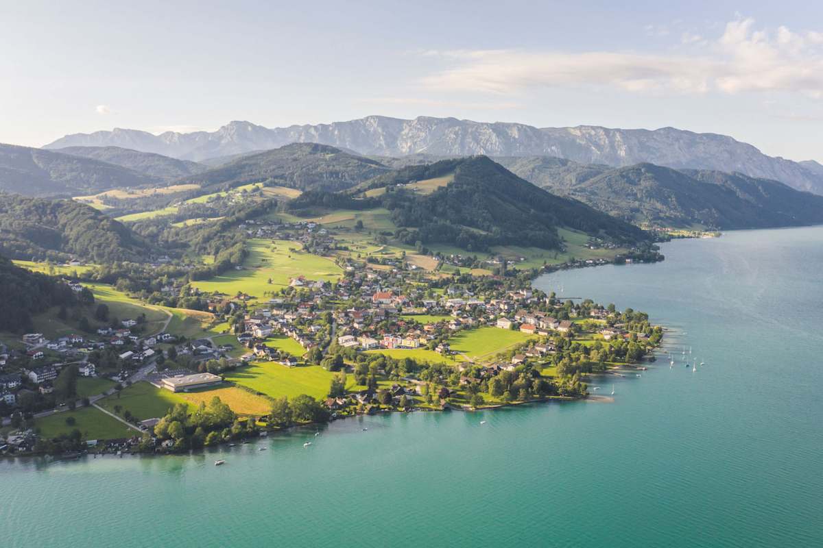 Ein kleiner Ort an einem türkisblauen See mit Bergen im Hintergrund.