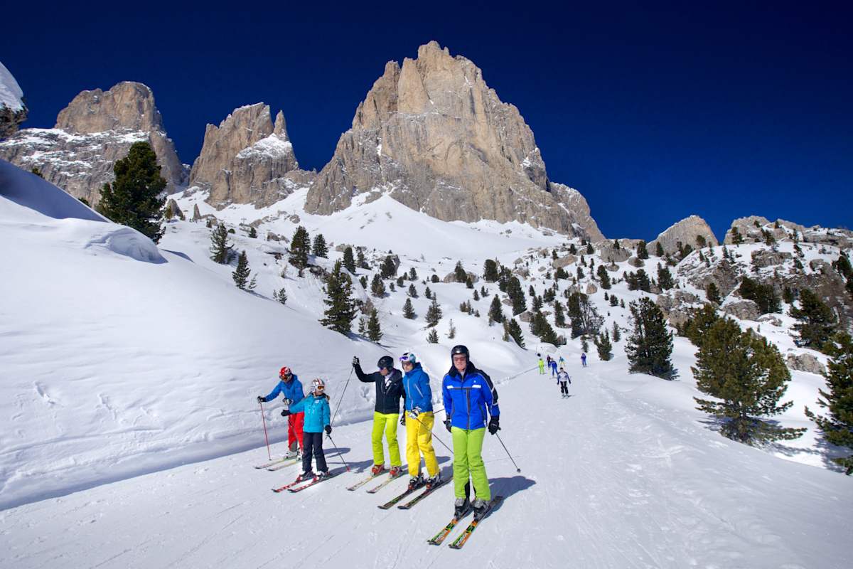 Fünf Skifahrer fahren die Sellaronda in Südtirol im Hintergrund ein schönes Dolomitenpanorama.