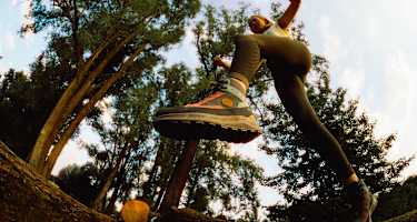 Frau springt im Wald über einen Baumstamm mit dem Hanwag Rotpunkt Light Mid GTX – leichter, vielseitiger Outdoor-Schuh für Alltag und Wanderungen